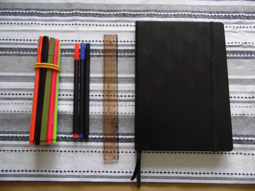 Coloured pens, ruler and a black notebook.